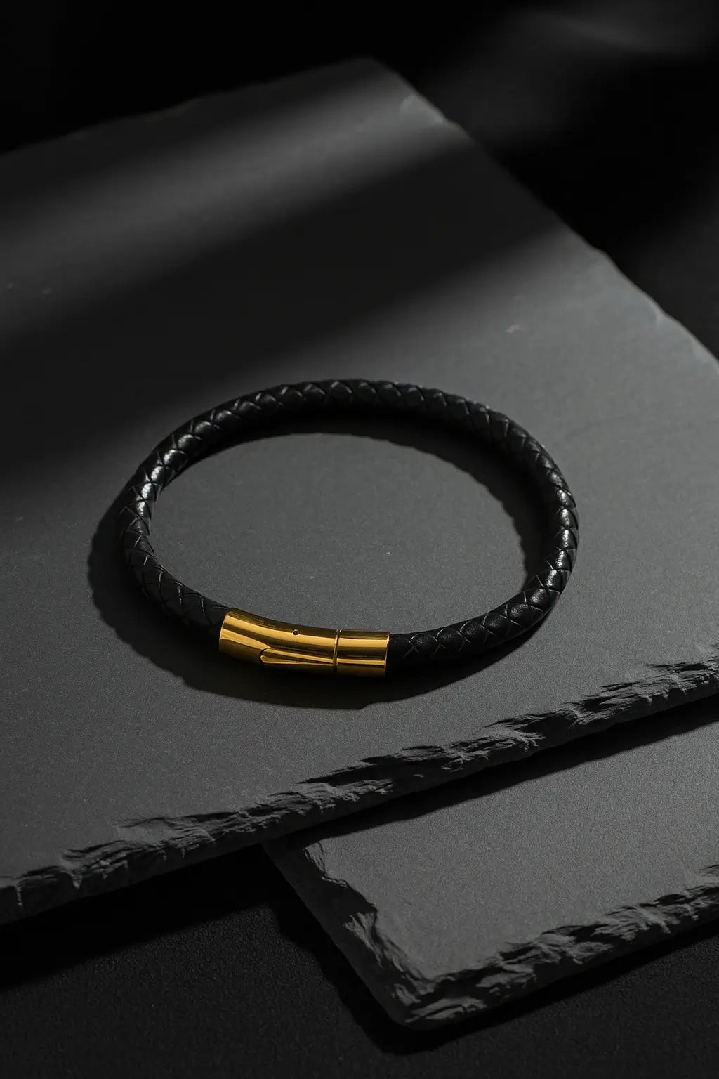 Black leather bracelet with gold clasp on a dark surface