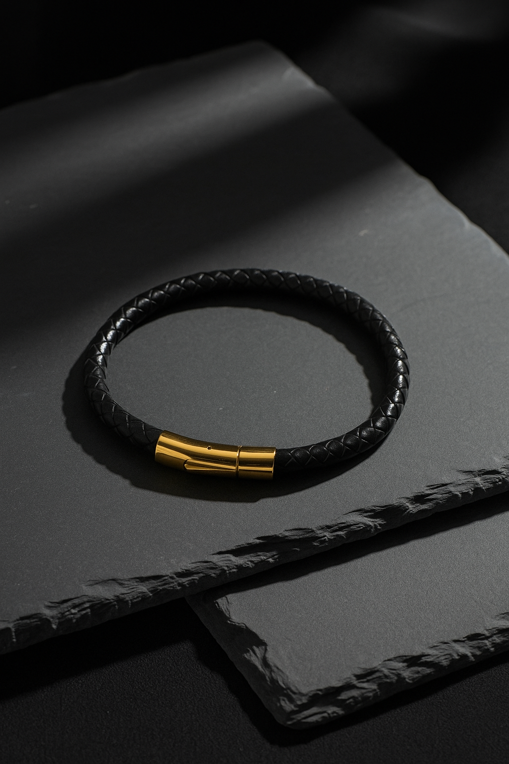 Black leather bracelet with gold clasp on a dark surface
