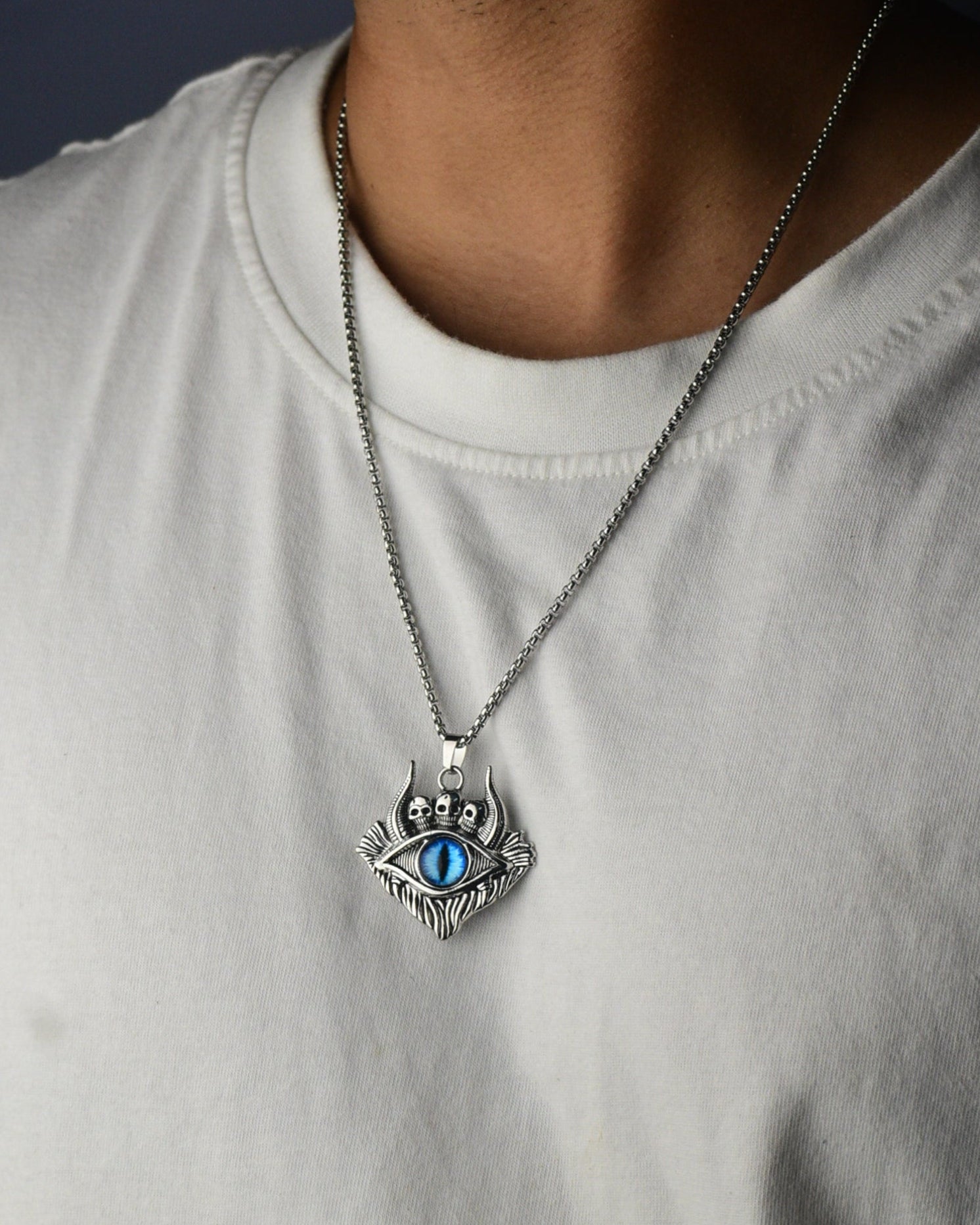 Person wearing a white sleeveless shirt with a silver necklace featuring an eye pendant.