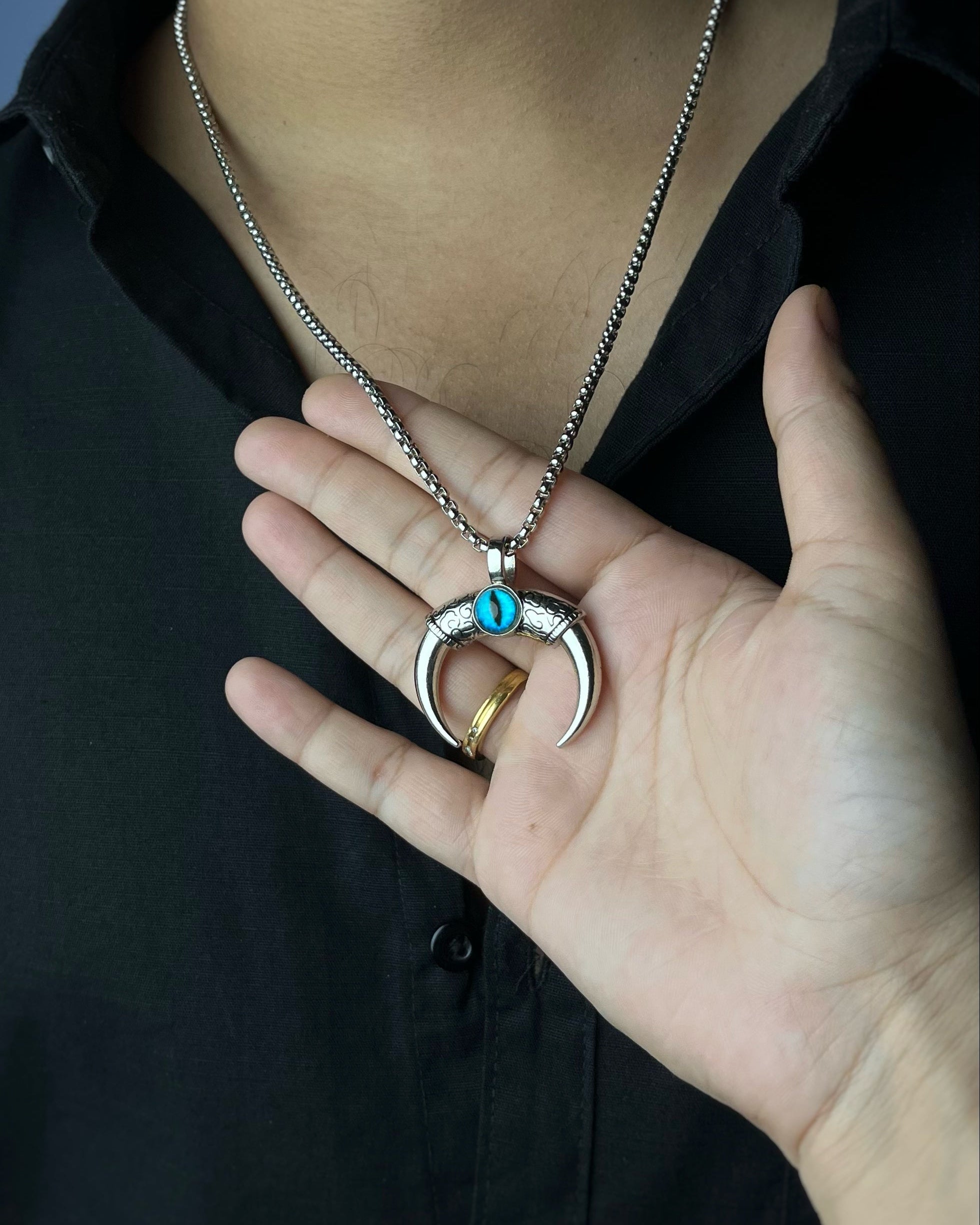Person holding a silver necklace with a unique pendant against a dark background