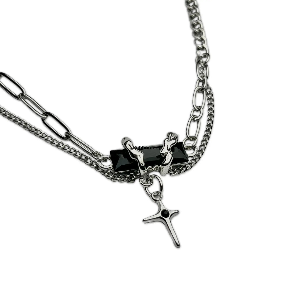 A silver-tone double-chain necklace featuring a central black rectangular block with a small silver figure and a dangling silver cross charm with a black center, shown on a plain white background.