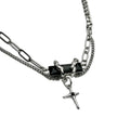 A silver-tone double-chain necklace featuring a central black rectangular block with a small silver figure and a dangling silver cross charm with a black center, shown on a plain white background.