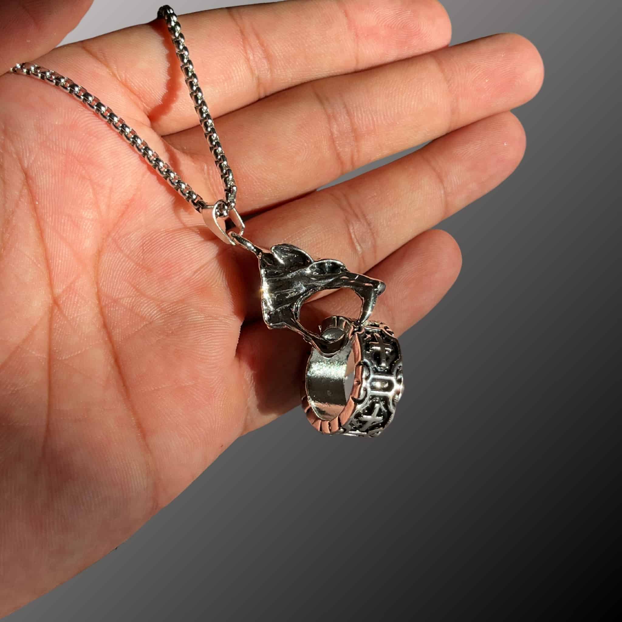 Hand holding a silver chain with a unique pendant against a gray background