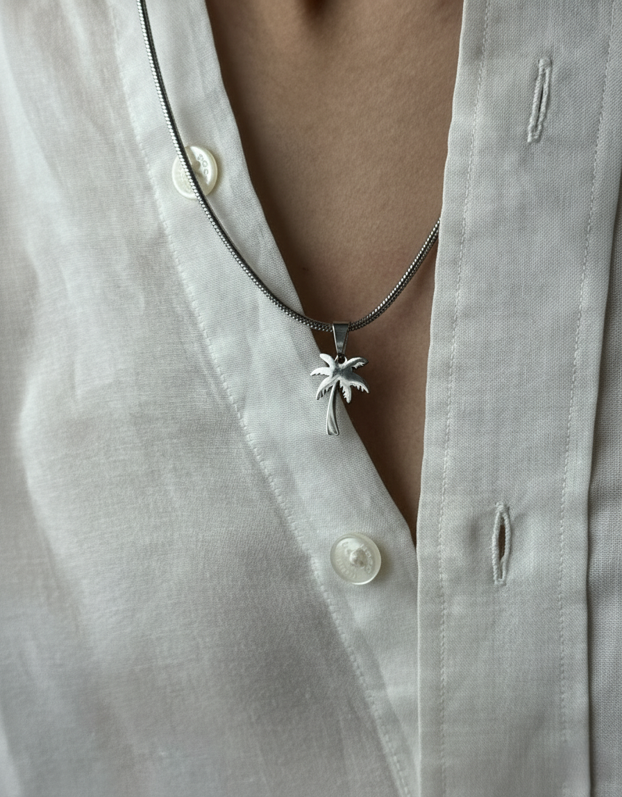 Necklace with a palm tree pendant worn by a person in a light-colored shirt.